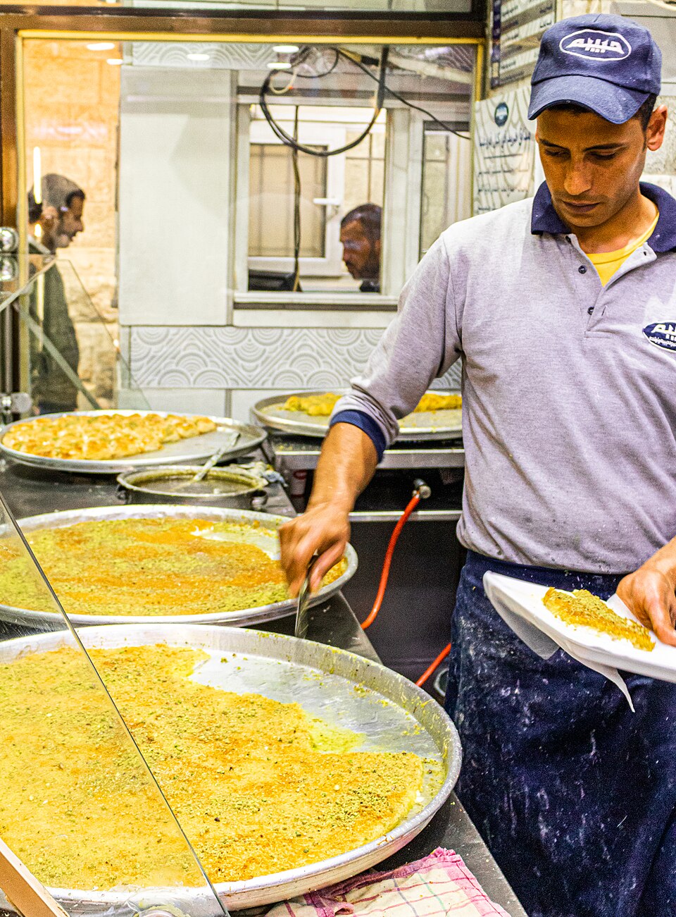 A Habibah Sweets server cutting knafeh from large round trays